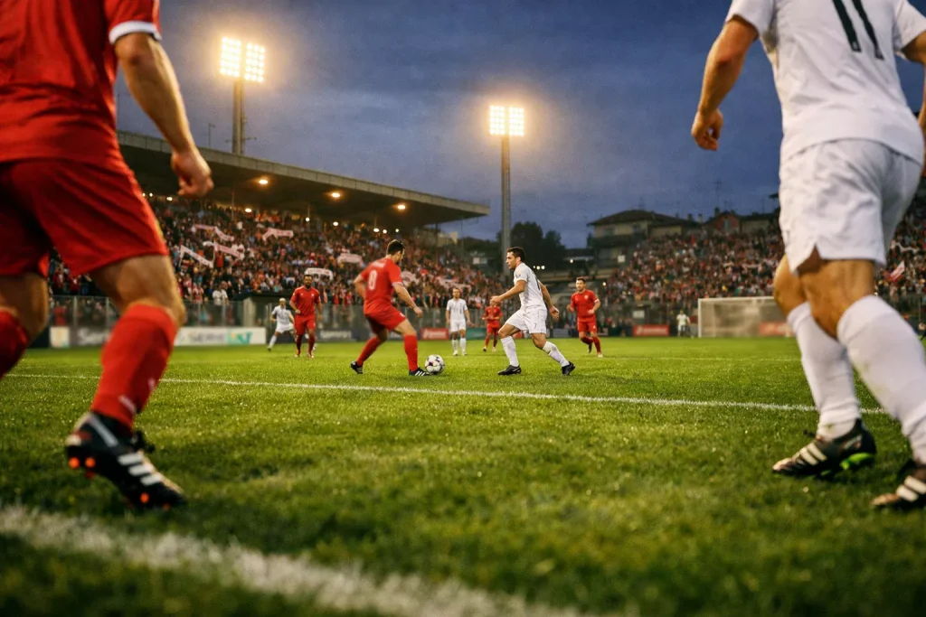 Campo da calcio di Serie B italiano illuminato durante una partita serale con tribune e tifosi